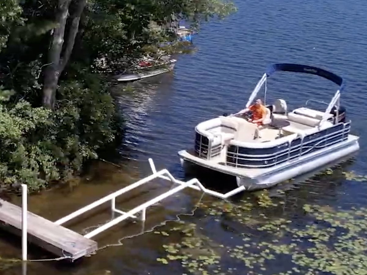 A pontoon boat approaching the open Docked guide arms at the end of a dock